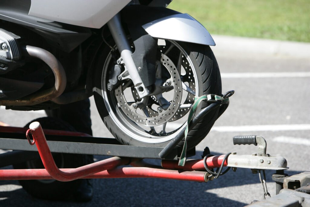 Roue avant de moto immobilisée dans le rail central rouge d'une remorque par le dépanneur après une panne sur la route